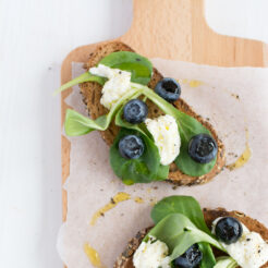 cropped image of two slices of bread adorned with fresh blueberries, caprese leaves, and mozzarella, drizzled with olive oil