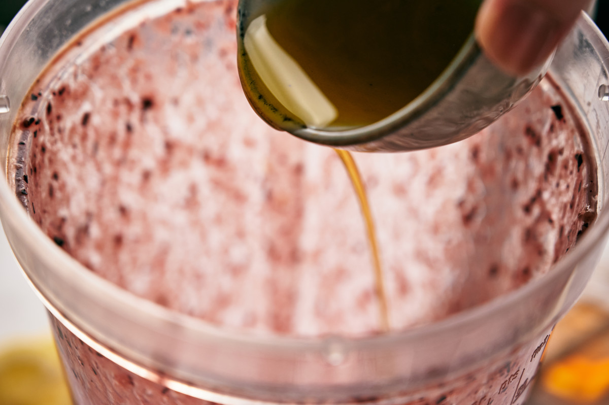 Pouring honey into a blender with blueberries.