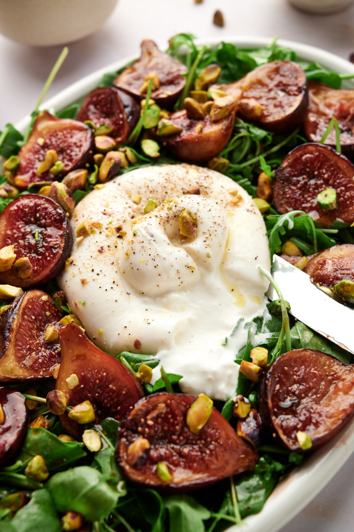 A closeup of a Fig & Arugula Salad with a knife cutting into a ball of Burrata.