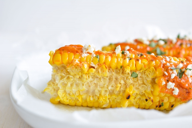 closer view of 2 Grilled Corns Topped with Lime Butter and Crumble Feta Cheese, and Fresh chopped Coriander 