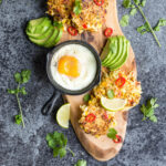 cropped image of spicy sweetcorn and potato fritters lay flat in the chopping board with sliced avocado and sunny side up egg